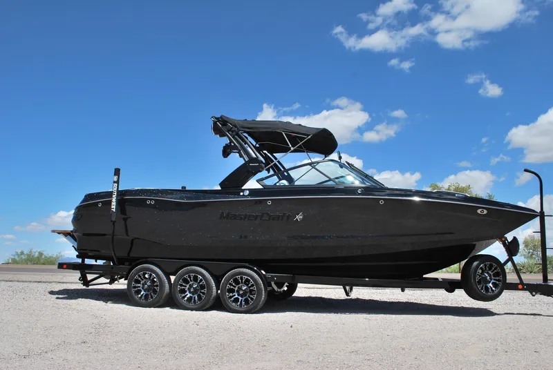 Slide: The Image of 2024 MasterCraft X26 boat on trailer under clear blue sky. - 1