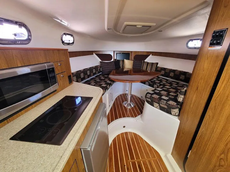 Slide: The Image of 2013 Pursuit 345 OS Offshore cabin with kitchenette, seating, and wood accents. - 26