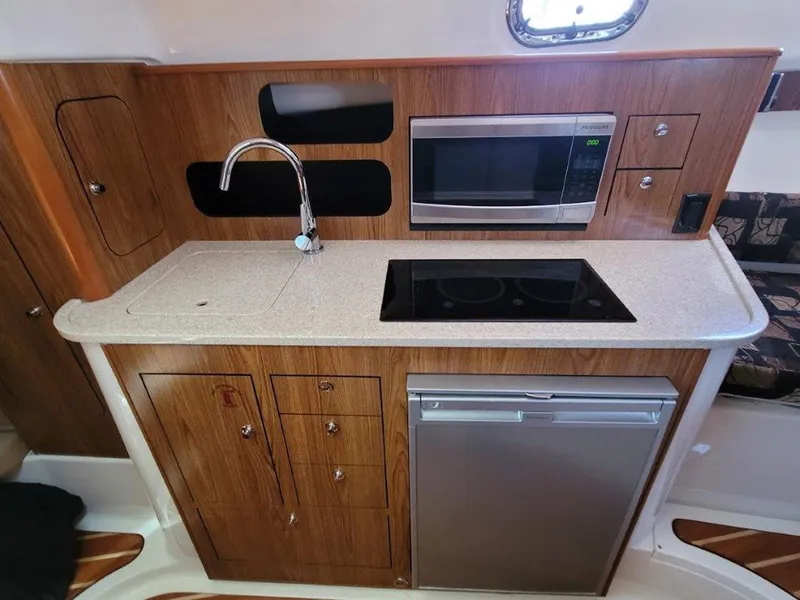 Slide: The Image of 2013 Pursuit 345 OS Offshore boat kitchen with wood cabinetry, sink, microwave, and stove. - 32