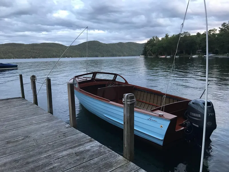 Slide: The Image of 1956 Lyman 18 Outboard boat docked on a serene lake with cloudy skies. - 11