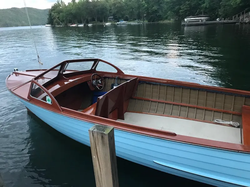 Slide: The Image of 1956 Lyman 18 Outboard boat docked on a serene lake with lush green surroundings. - 13