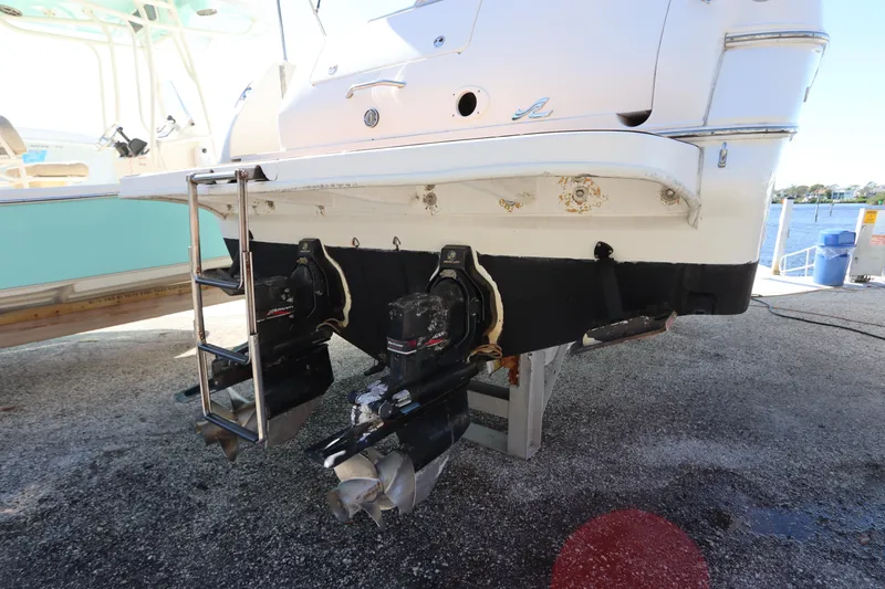 Slide: The Image of 2001 Sea Ray 310 Sundancer boat with dual outboard motors and ladder, docked on land. - 2