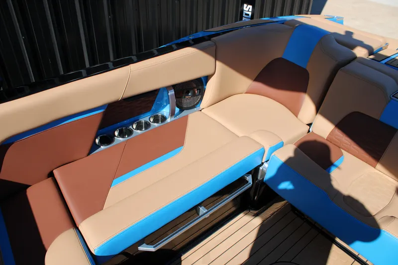 Slide: The Image of 2023 MasterCraft X26 interior with tan and blue seating, cup holders, and teak flooring. - 13
