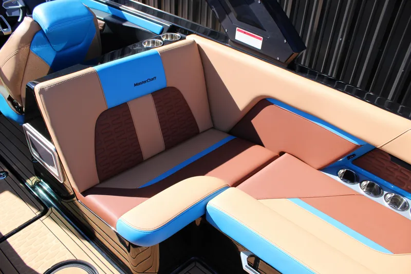 Slide: The Image of 2023 MasterCraft X26 boat interior with tan and blue seating, cup holders, and sleek design. - 15