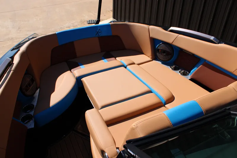 Slide: The Image of 2023 MasterCraft X26 boat interior with tan and blue seating, cup holders, and speakers. - 21