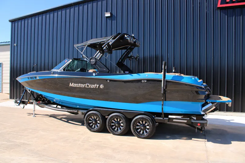 Slide: The Image of 2023 MasterCraft X26 boat on trailer, black and blue design, parked outside a building. - 5