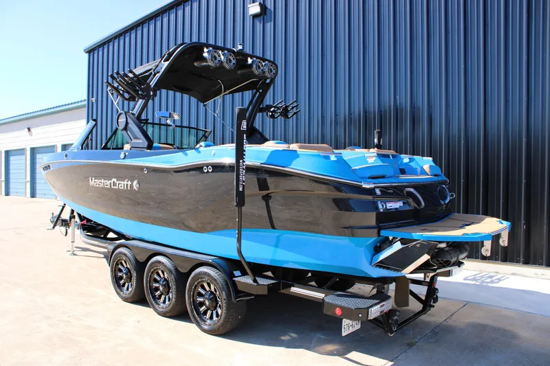 Slide: The Image of 2023 MasterCraft X26 boat on trailer, blue and black design, parked near a building. - 6