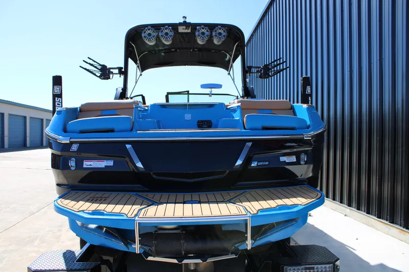 Slide: The Image of 2023 MasterCraft X26 boat with blue and black design, docked near a metal building. - 7