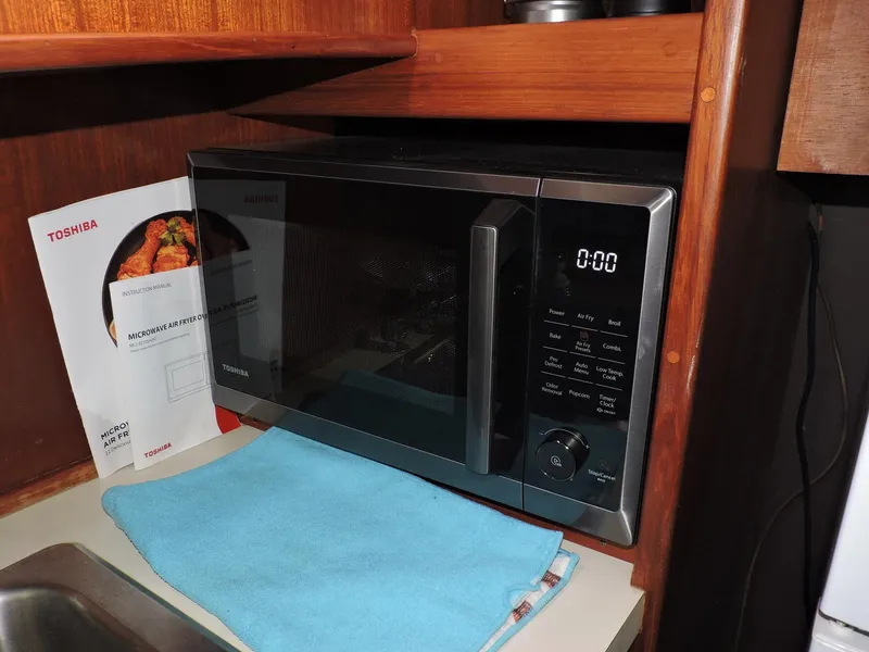 Slide: The Image of Microwave oven in wooden kitchen cabinet, with a blue cloth and cookbook nearby. - 29