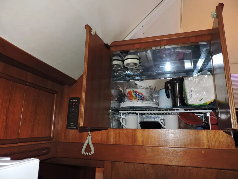 Slide: The Image of Wooden kitchen cabinet with open doors, displaying mugs, plates, and kitchenware. Post 44, 1990 model. - 34