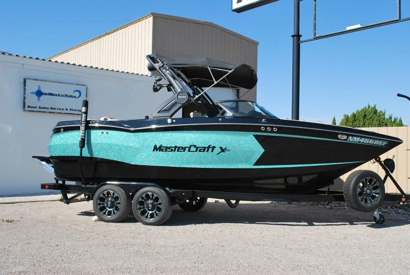 The Image of 2022 MasterCraft XStar boat on trailer, turquoise and black design, parked outdoors. - 0