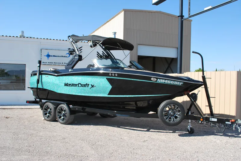 Slide: The Image of 2022 MasterCraft XStar boat on trailer, turquoise and black design, parked outdoors. - 1