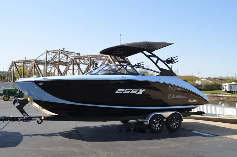 Slide: The Image of 2025 Yamaha Boats 255XD on trailer, sleek black design, parked near a bridge. - 2