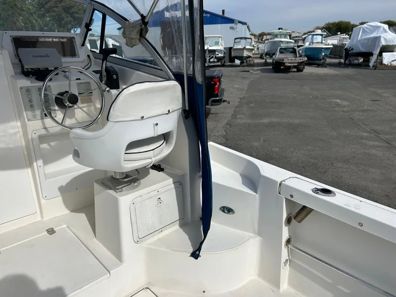 Slide: The Image of 1998 Cobia 220 Walkaround boat interior with steering wheel and seating in a marina. - 9