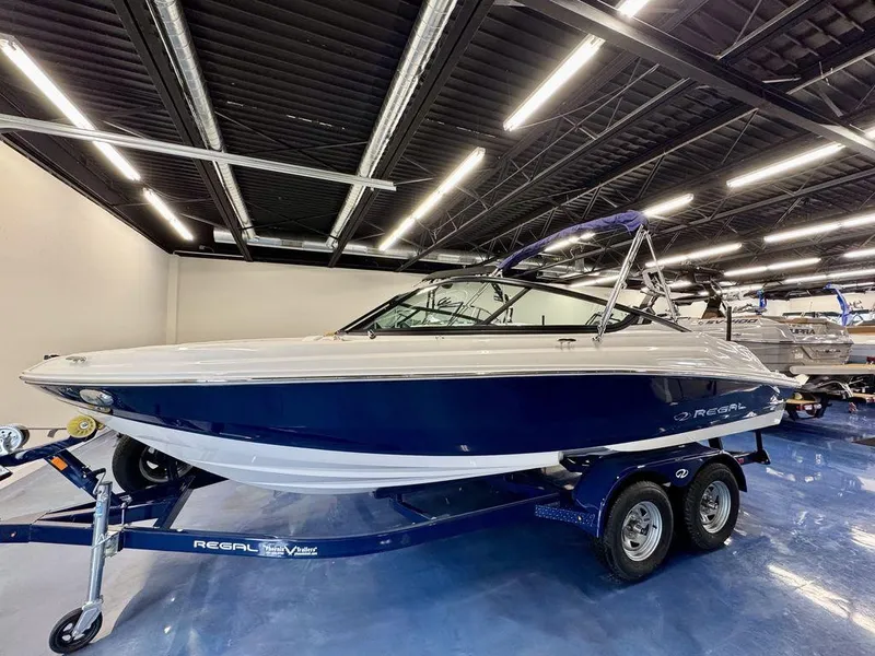 Slide: The Image of 2025 Regal 2000 ES boat on trailer in showroom, blue and white design. - 0