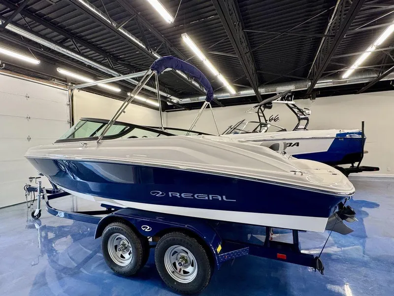 Slide: The Image of 2025 Regal 2000 ES boat on trailer in showroom, featuring sleek design and blue accents. - 1
