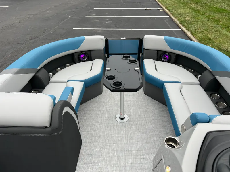 Slide: The Image of 2025 South Bay S224UL pontoon boat interior with blue and gray seating, cup holders, and table. - 22