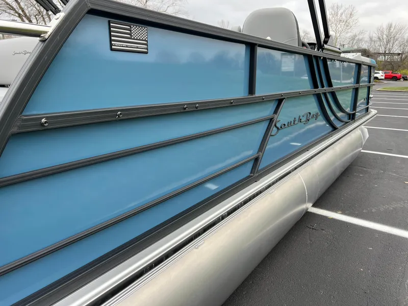 Slide: The Image of 2025 South Bay S224UL pontoon boat with blue paneling and American flag detail. - 6