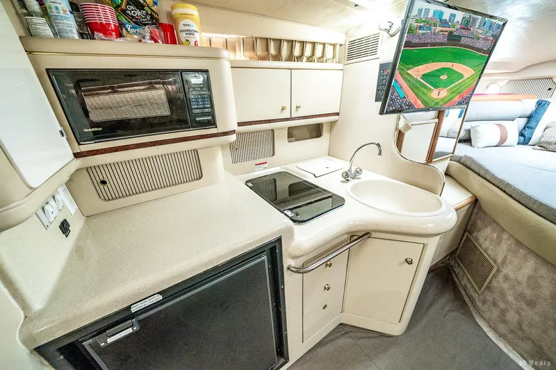 Slide: The Image of 1998 Sea Ray 330 Sundancer interior with kitchenette, microwave, sink, and TV showing baseball. - 38