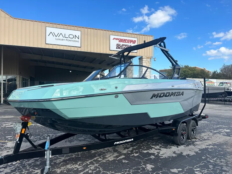 The Image of 2025 Moomba Max boat on trailer, parked outside dealership under blue sky. - 0
