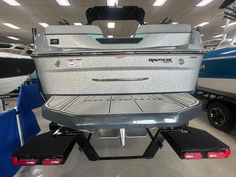 Slide: The Image of 2025 Moomba Max boat rear view in showroom, featuring swim platform and trailer. - 12