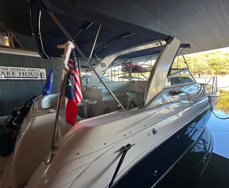 The Image of 2003 Rinker Fiesta Vee 312 boat docked at a lake house with flags displayed. - 0