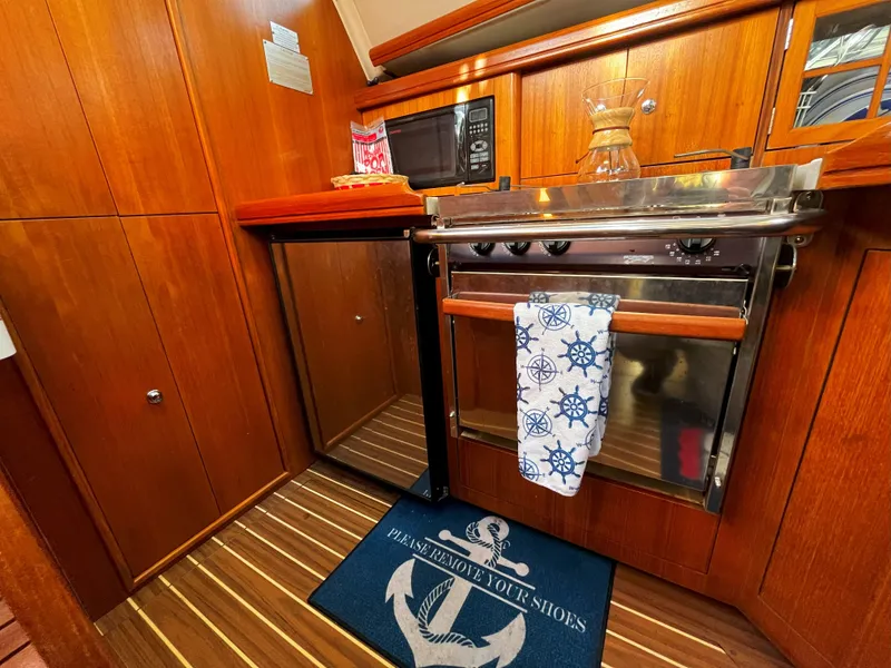 Slide: The Image of 2005 Hunter 41 yacht kitchen with wood cabinetry, stove, microwave, and nautical-themed decor. - 26
