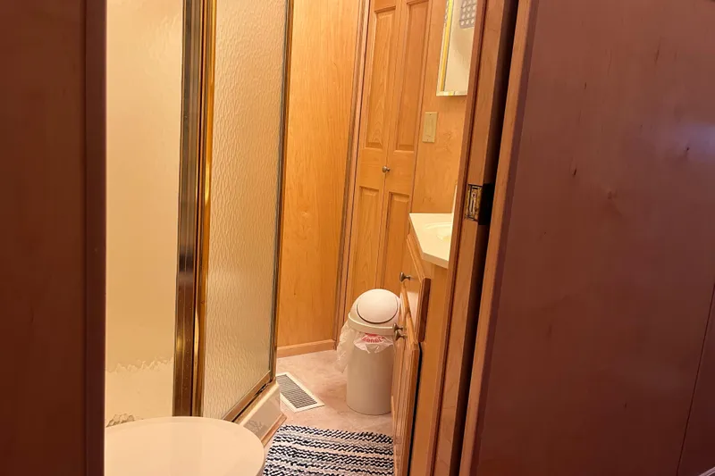 Slide: The Image of Compact bathroom with shower, wooden cabinets, and striped rug in a 2001 Sharpe 75 model. - 24