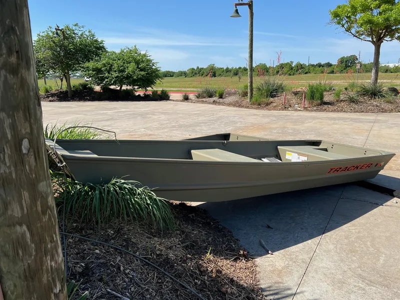 Slide: The Image of 2025 Tracker Grizzly 1436 Utility boat on concrete driveway, surrounded by greenery. - 0