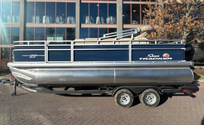 The Image of 2025 Sun Tracker Fishin' Barge 20 DLX pontoon boat on trailer, parked outdoors. - 0