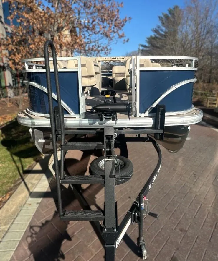 Slide: The Image of 2025 Sun Tracker Fishin' Barge 20 DLX pontoon boat on trailer, parked outdoors. - 2
