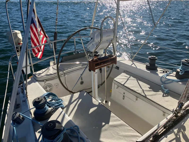 Slide: The Image of 1983 Morgan Nelson Marek 454 sailboat cockpit with steering wheel, ropes, and American flag on water. - 2