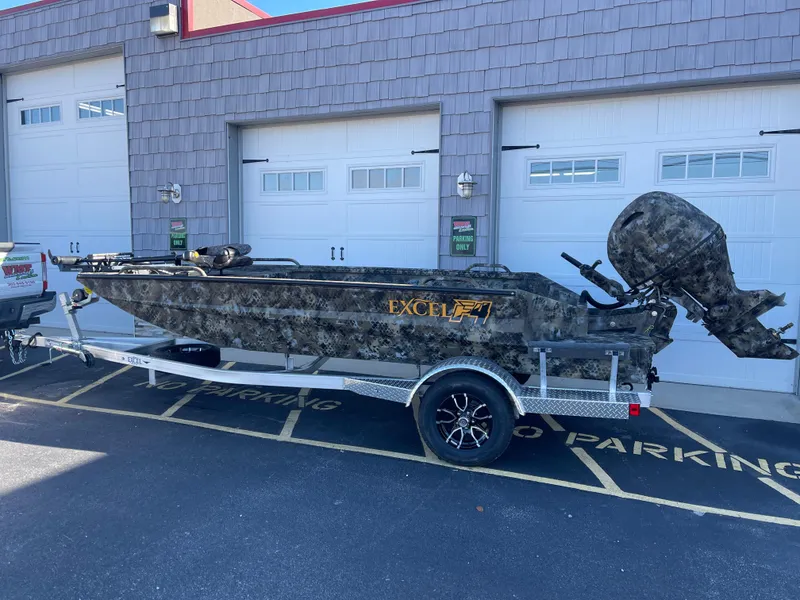 Slide: The Image of 2025 Excel 1860 F4 Shallow Water boat on trailer, camo design, parked outside garage. - 2
