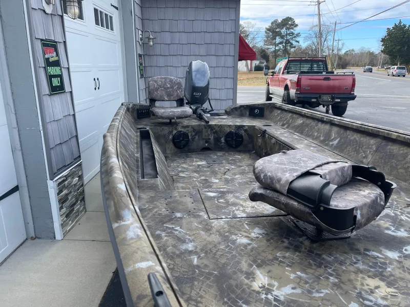 Slide: The Image of 2025 Excel 1751 River Warrior boat with camo seats, parked near a garage. - 5