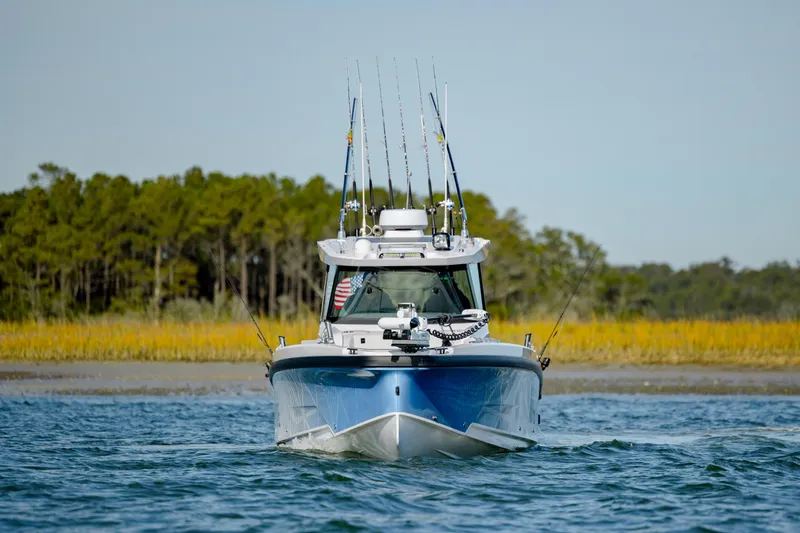 Slide: The Image of 2025 Axopar 29 CCX boat on water, equipped with fishing rods, forested shoreline in background. - 4