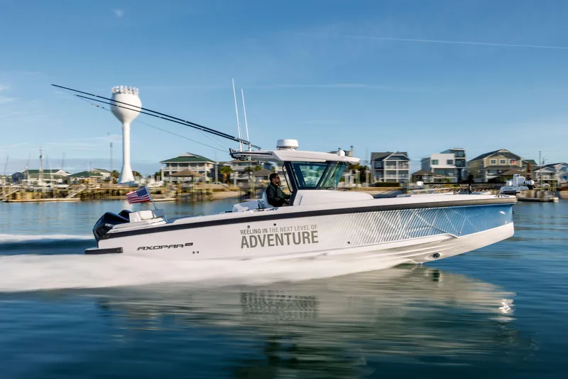 Slide: The Image of 2025 Axopar 29 CCX boat cruising on calm water near coastal town. - 42
