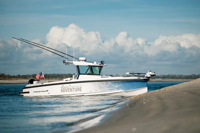 Slide: The Image of 2025 Axopar 29 CCX boat on sandy shore with American flag, under blue sky. - 43