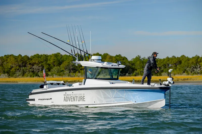 Slide: The Image of 2025 Axopar 29 CCX boat on water, person fishing, lush green background. - 5