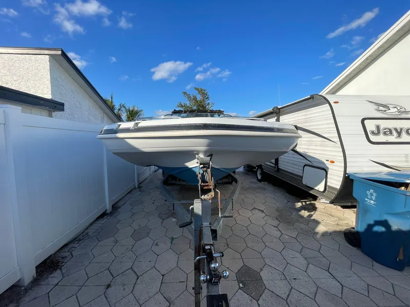 Slide: The Image of 2001 Hurricane 232 OB boat on trailer, parked beside RV under clear blue sky. - 1