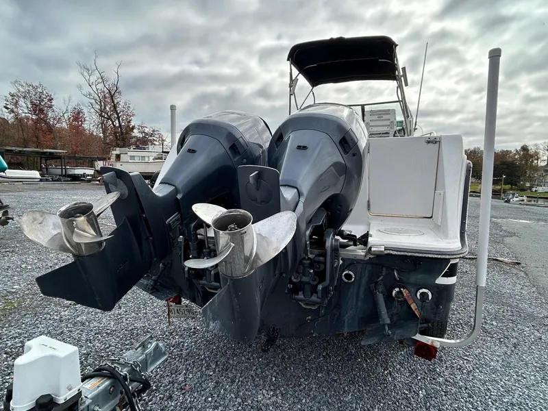 Slide: The Image of 1996 Robalo 2440 Walkaround boat with dual outboard motors, parked on gravel. - 5