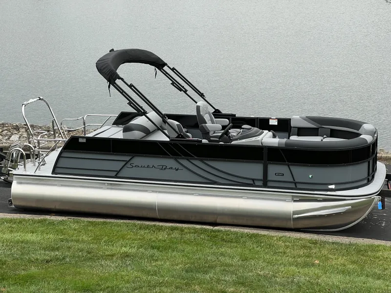 Slide: The Image of 2025 South Bay S222 UL pontoon boat on a grassy shoreline. - 1