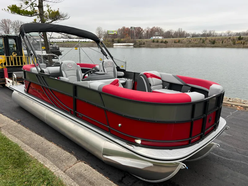 Slide: The Image of 2025 South Bay S222 RS Tri 3.0 pontoon boat with red and gray seating by a lake. - 3