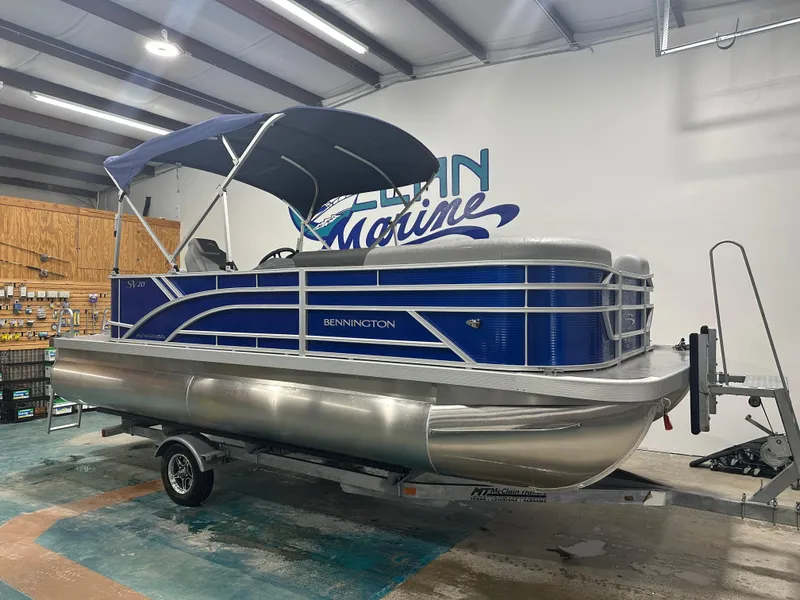 Slide: The Image of 2024 Bennington 20SVLSR pontoon boat with blue canopy on trailer in showroom. - 1
