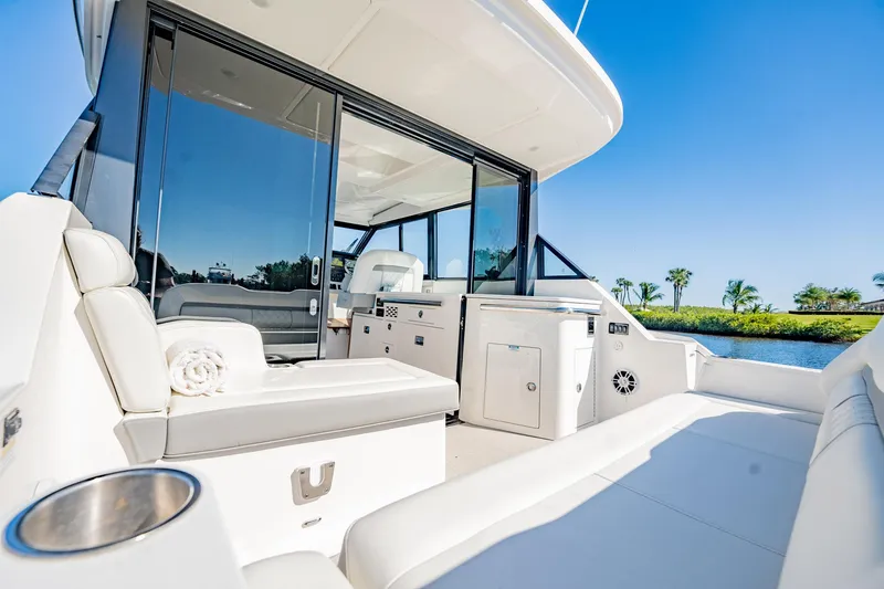 Slide: The Image of 2022 Regal 36 XO yacht with sleek interior and outdoor seating, set against a sunny waterfront. - 22