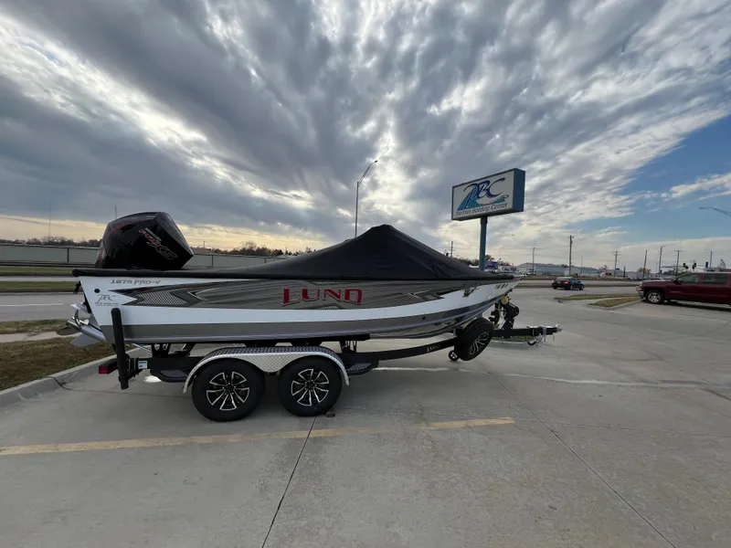 Slide: The Image of 2024 Lund 1875 Pro-V boat on trailer under dramatic cloudy sky. - 2