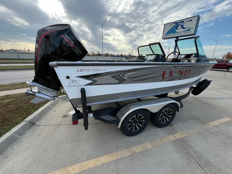 Slide: The Image of 2024 Lund 1875 Pro-V boat on trailer, parked outdoors under cloudy sky. - 7