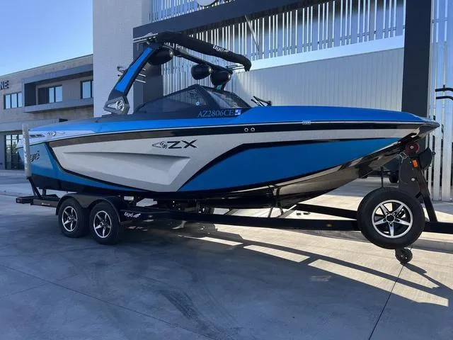 Slide: The Image of 2020 Tigé 23ZX boat on trailer, blue and white design, parked outdoors. - 2
