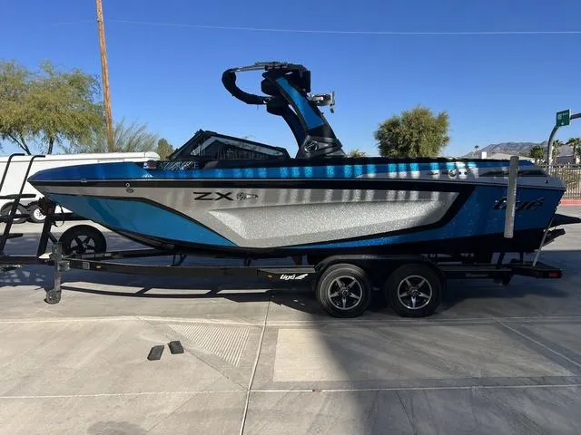 Slide: The Image of 2020 Tigé 23ZX boat on trailer, blue and silver design, parked outdoors. - 5
