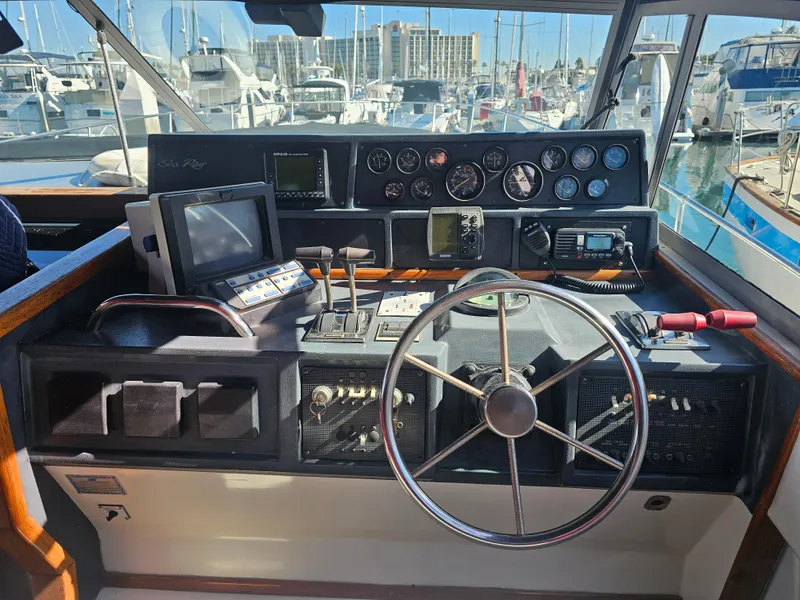 Slide: The Image of 1988 Sea Ray 390 Express Cruiser helm with navigation instruments and steering wheel in marina setting. - 24