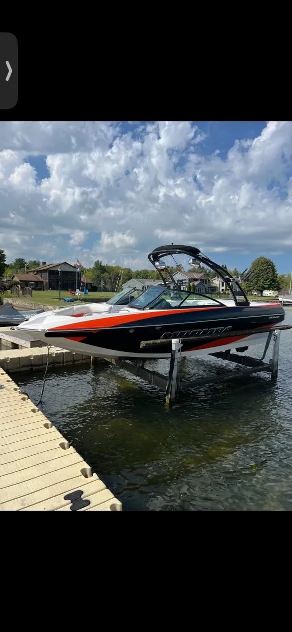 Slide: The Image of 2014 Moomba Mondo boat on lift by dock, under a partly cloudy sky. - 6
